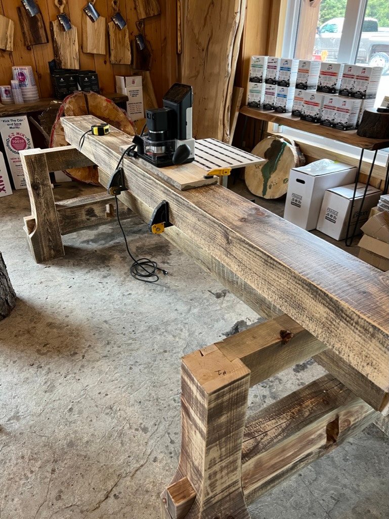 Layered timber conference-table base during construction, with a router setup on its long beam