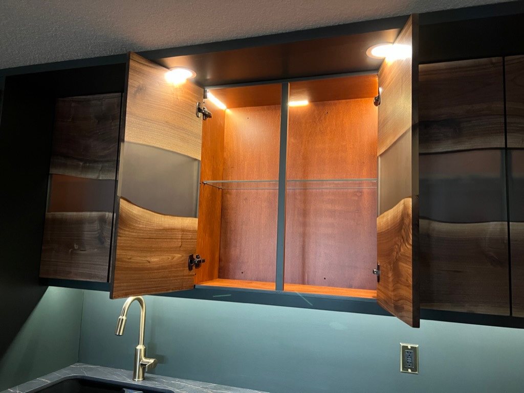 Installed wet-bar upper cabinet open to show its walnut interior, shelving rails and lighting